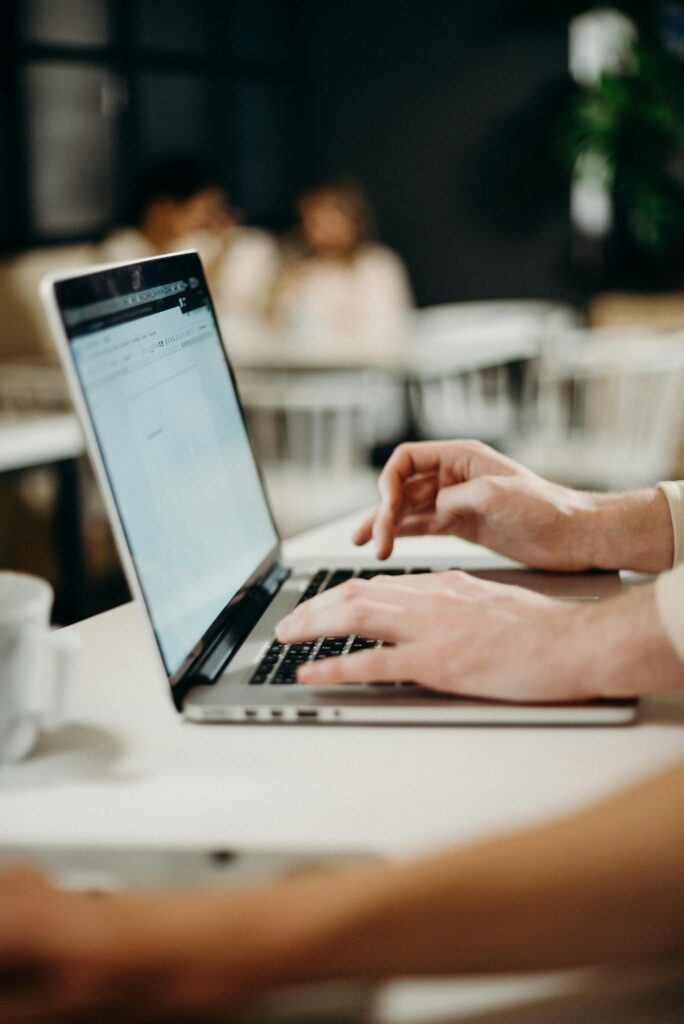 Close-up of hands typing on a laptop in a cozy indoor cafe setting.