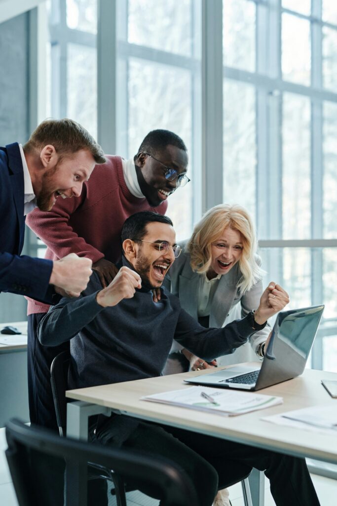 pexels-photo-7108959-7108959 A diverse team in an office celebrates a successful achievement while looking at a laptop.