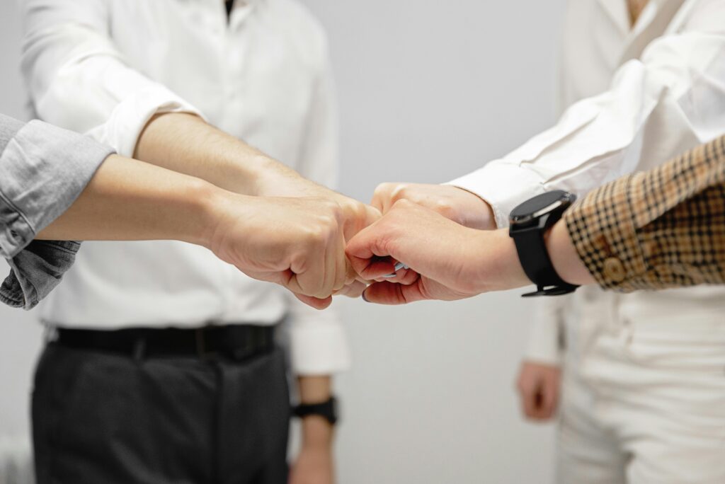 pexels-photo-7989232-7989232 Close-up of diverse team members doing a fist bump indoors, symbolizing unity and teamwork.